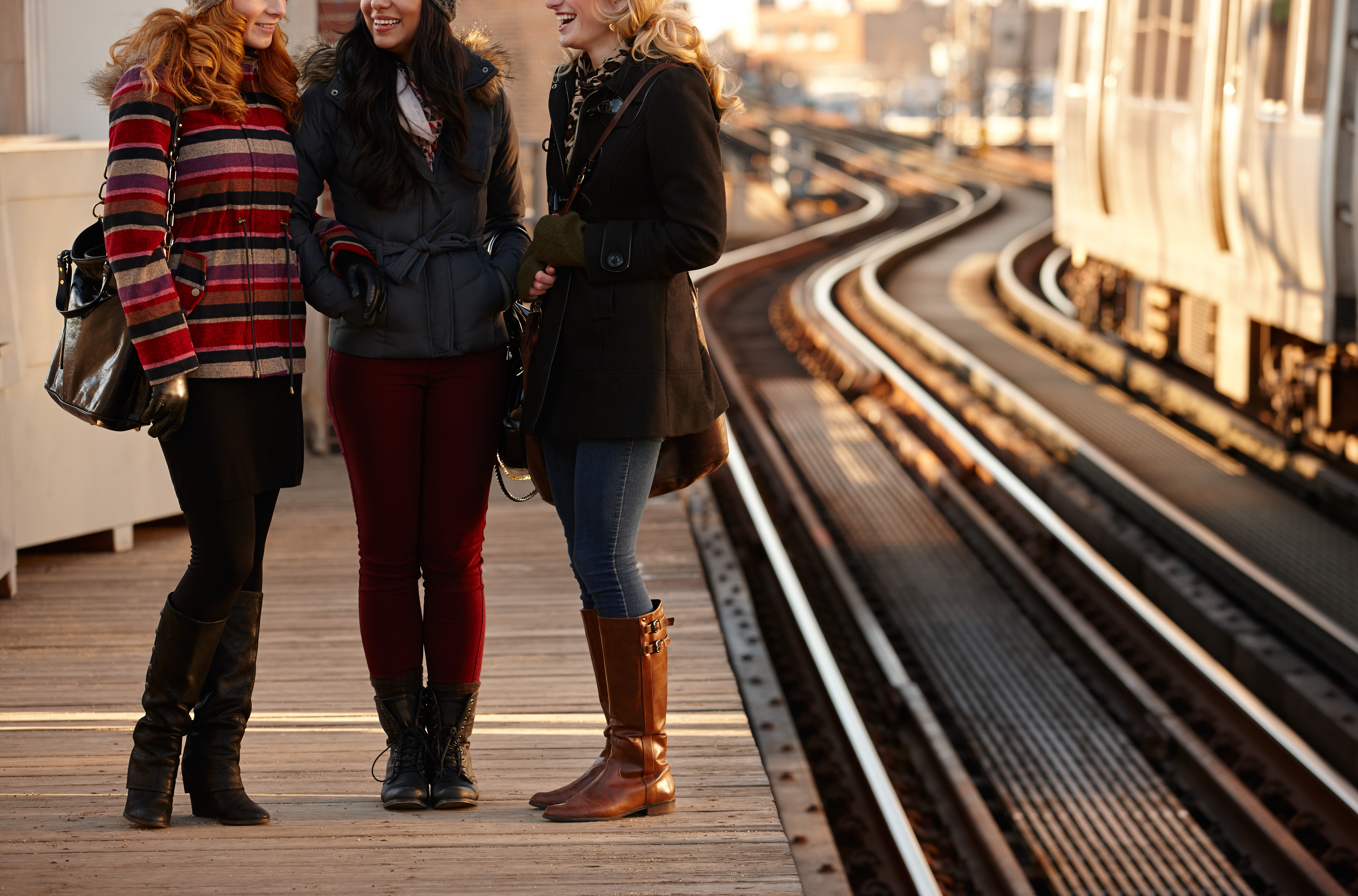 3 women standing on a platform and talking while waiting for a train to arrive