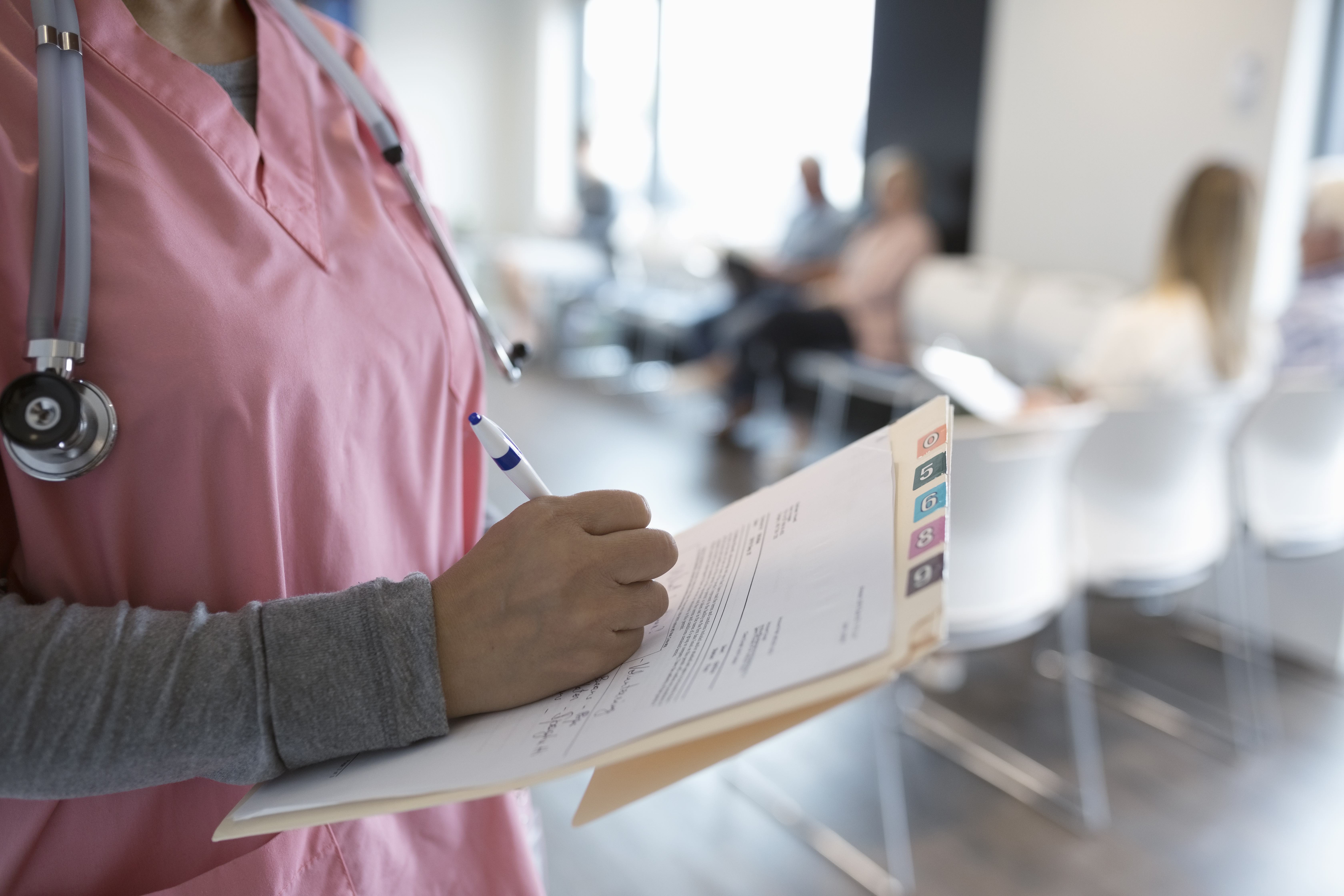 medical provider in pink scrubs writing in a chart