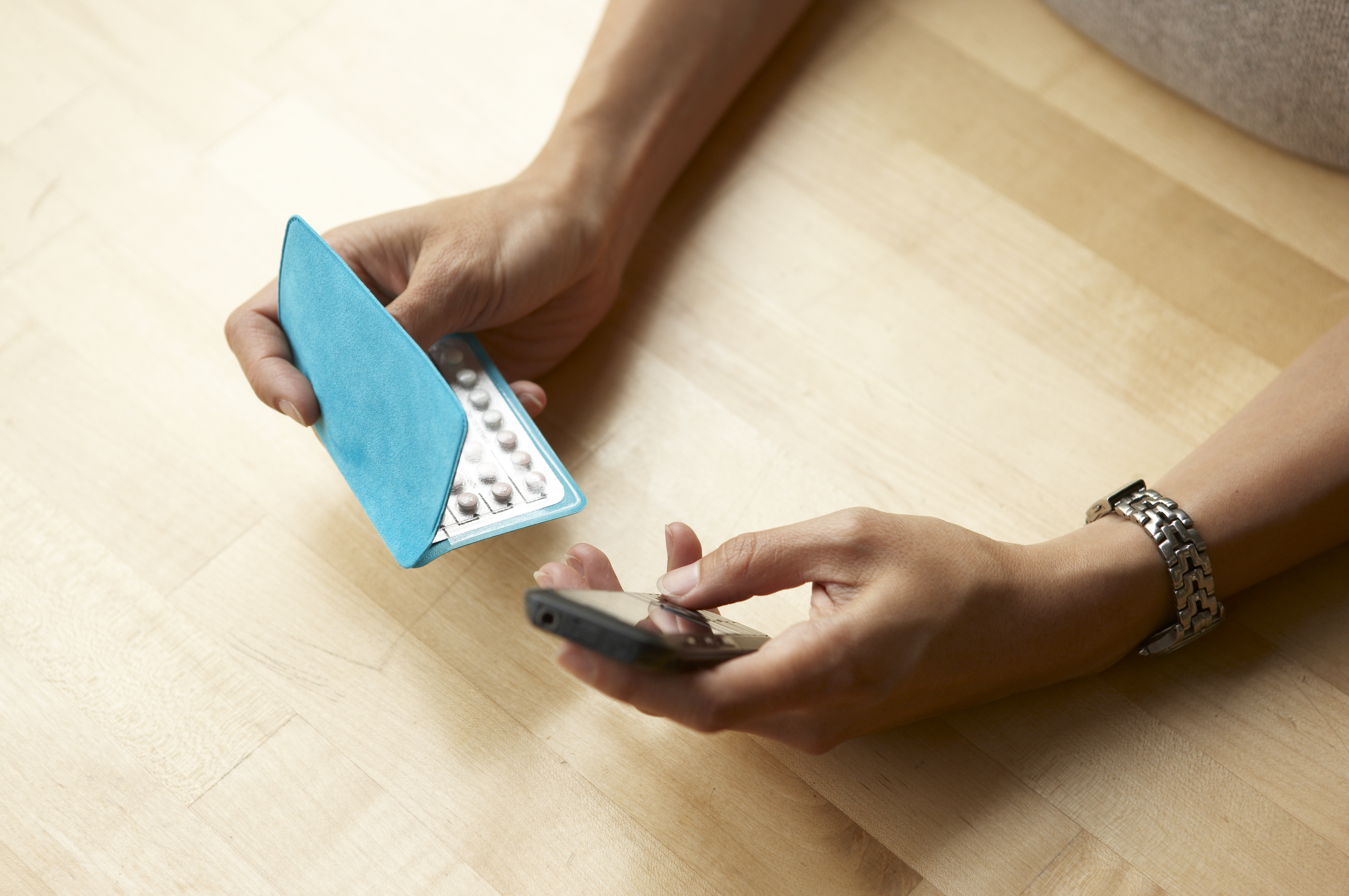 bird's eye view of a person holding a monthly pack of oral contraceptives in one hand and a cell phone in the other