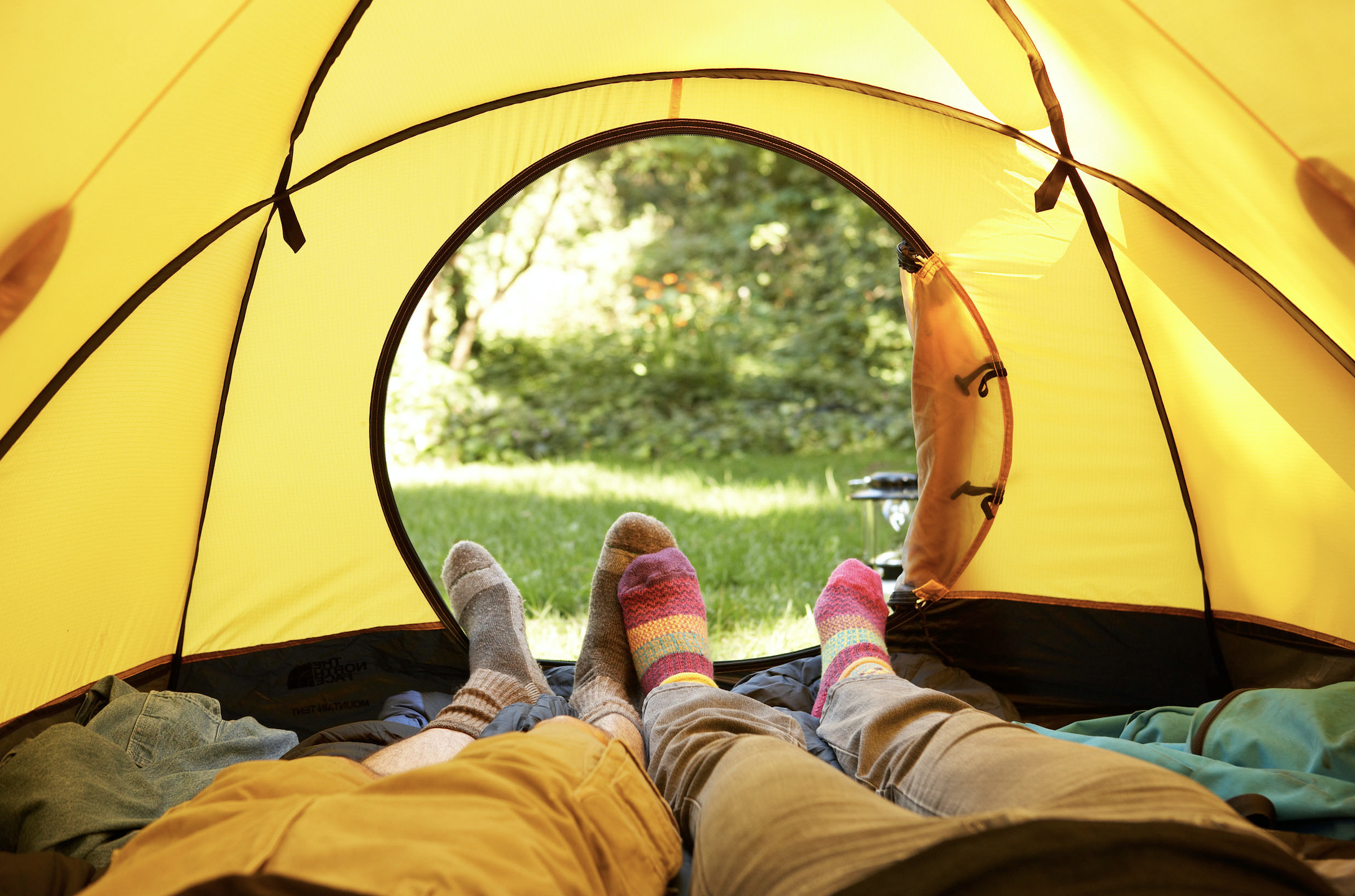 two pairs of legs lying down in a yellow tent facing the tent entrance