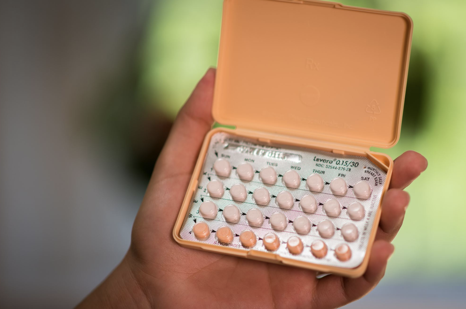 a hand holding an orange monthly pack of oral contraceptives