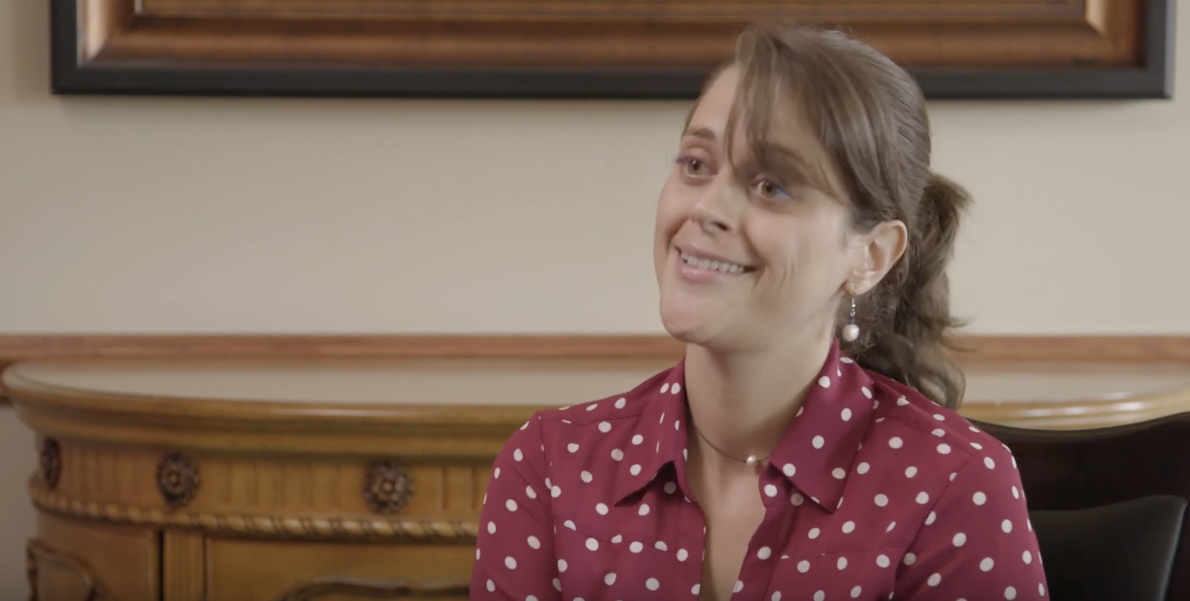 white woman with brown hair and a red and white polka dot shirt being interviewed