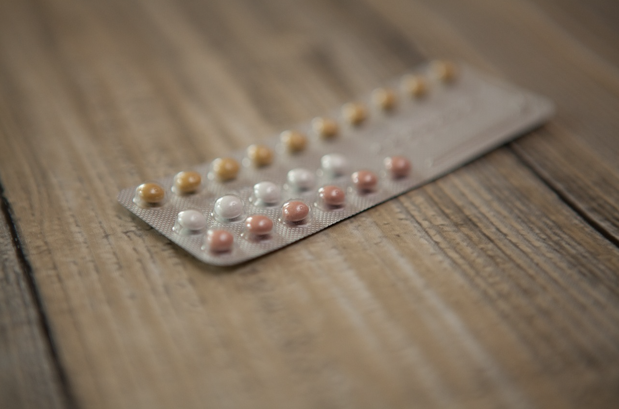 close up of yellow, white, and red oral contraceptives on a wooden surface