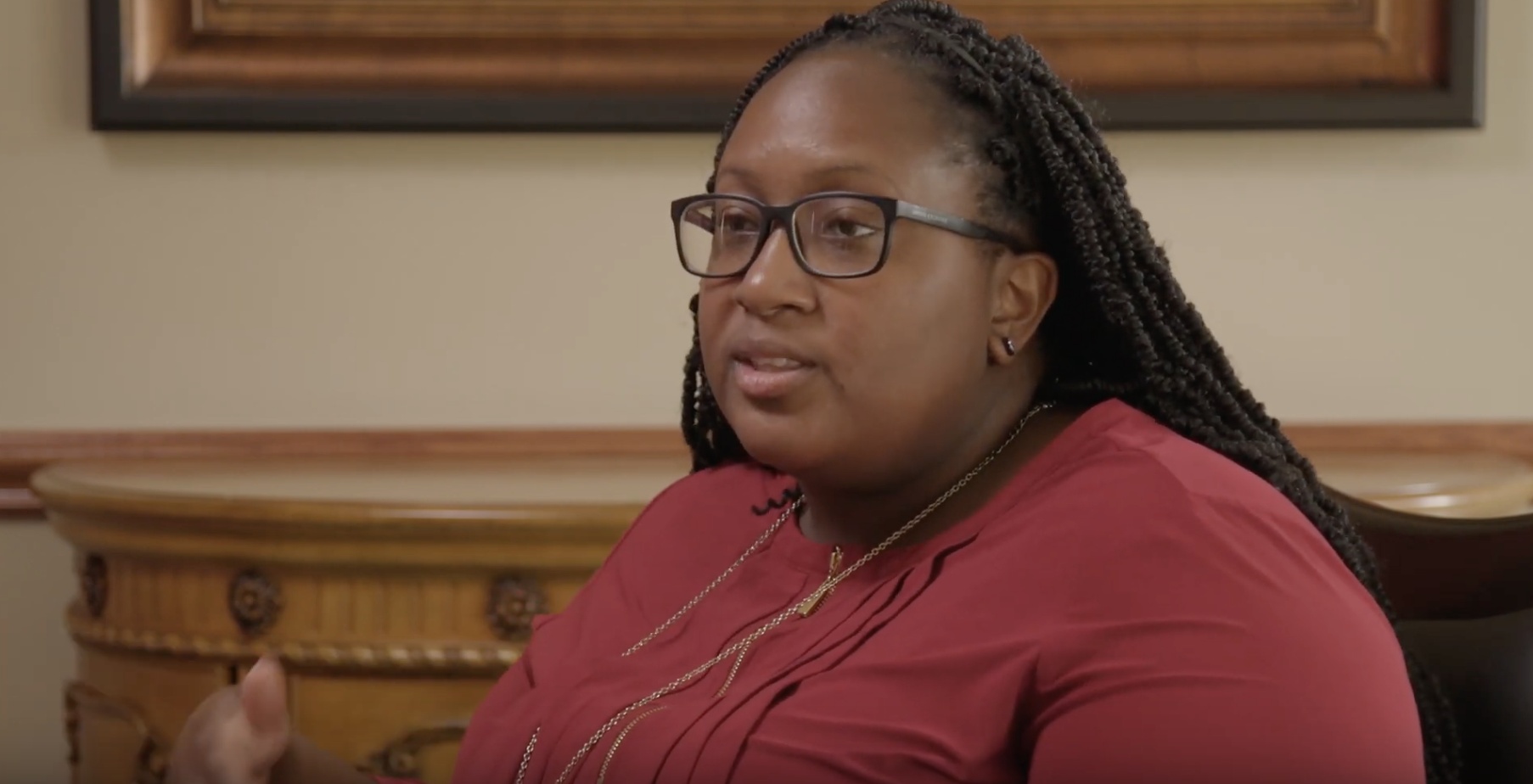 BIPOC woman in a red shirt and glasses being interviewed