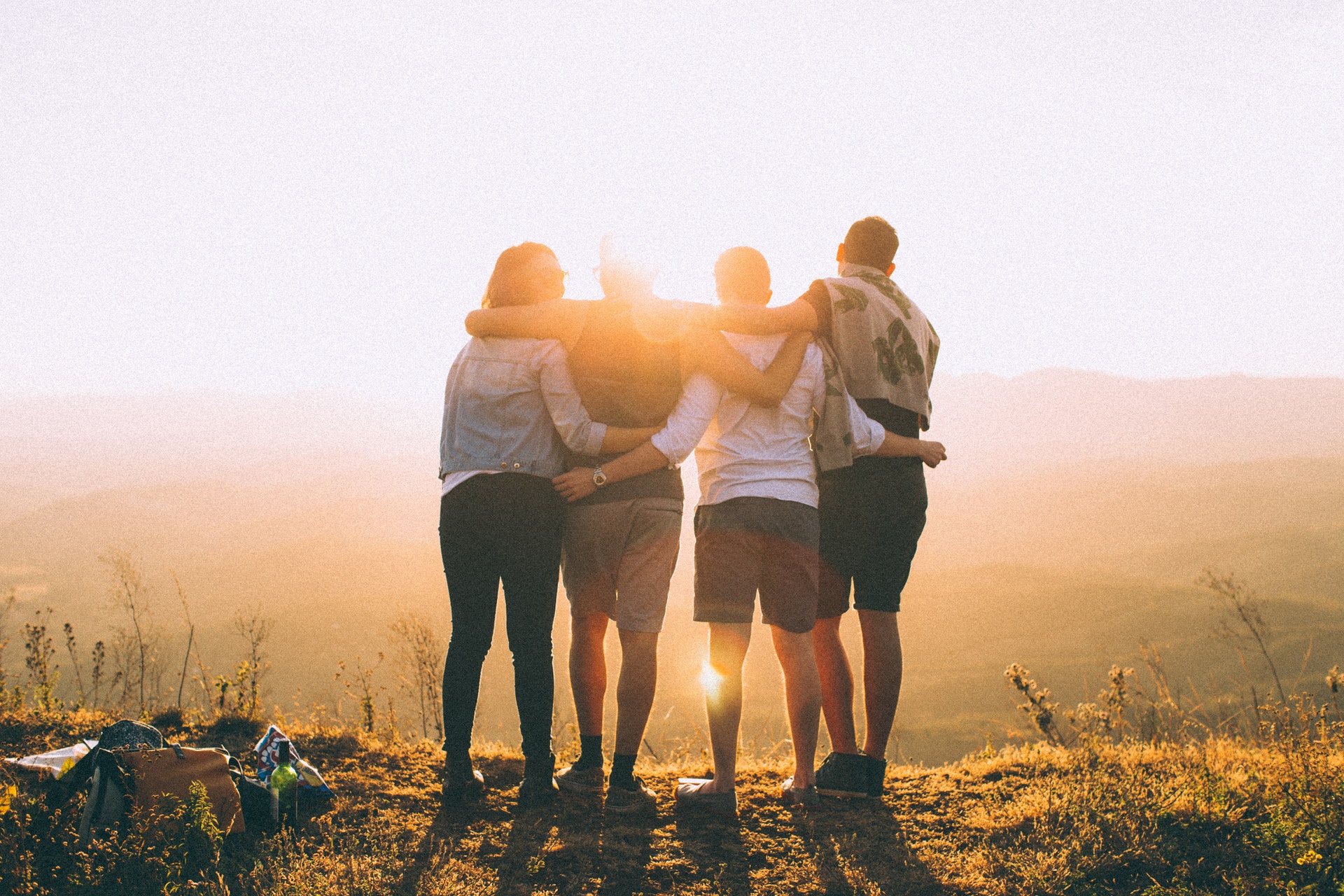 four friends with their arms around each other on a mountain at sunset