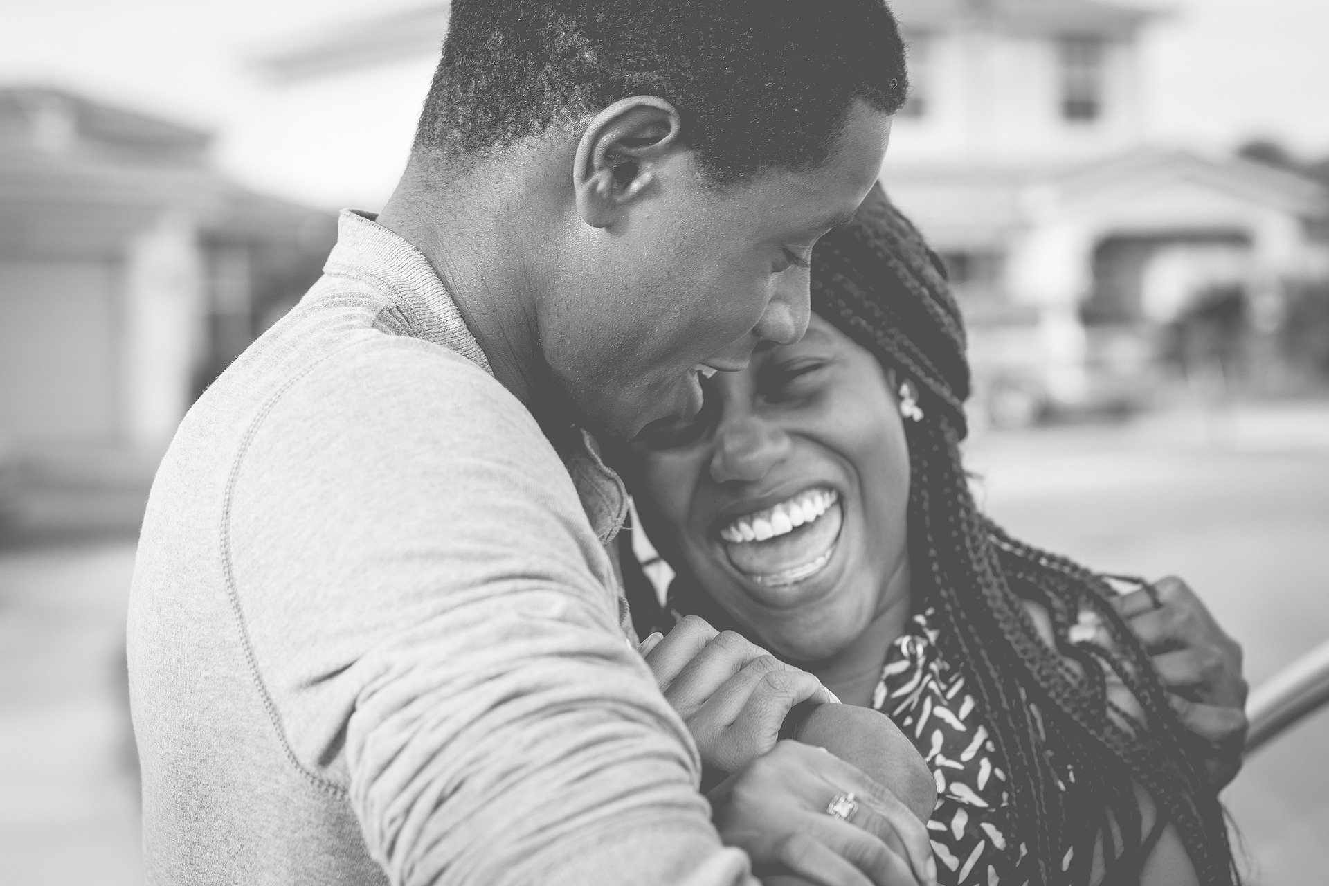 black and white image of BIPOC couple laughing and snuggling on the street