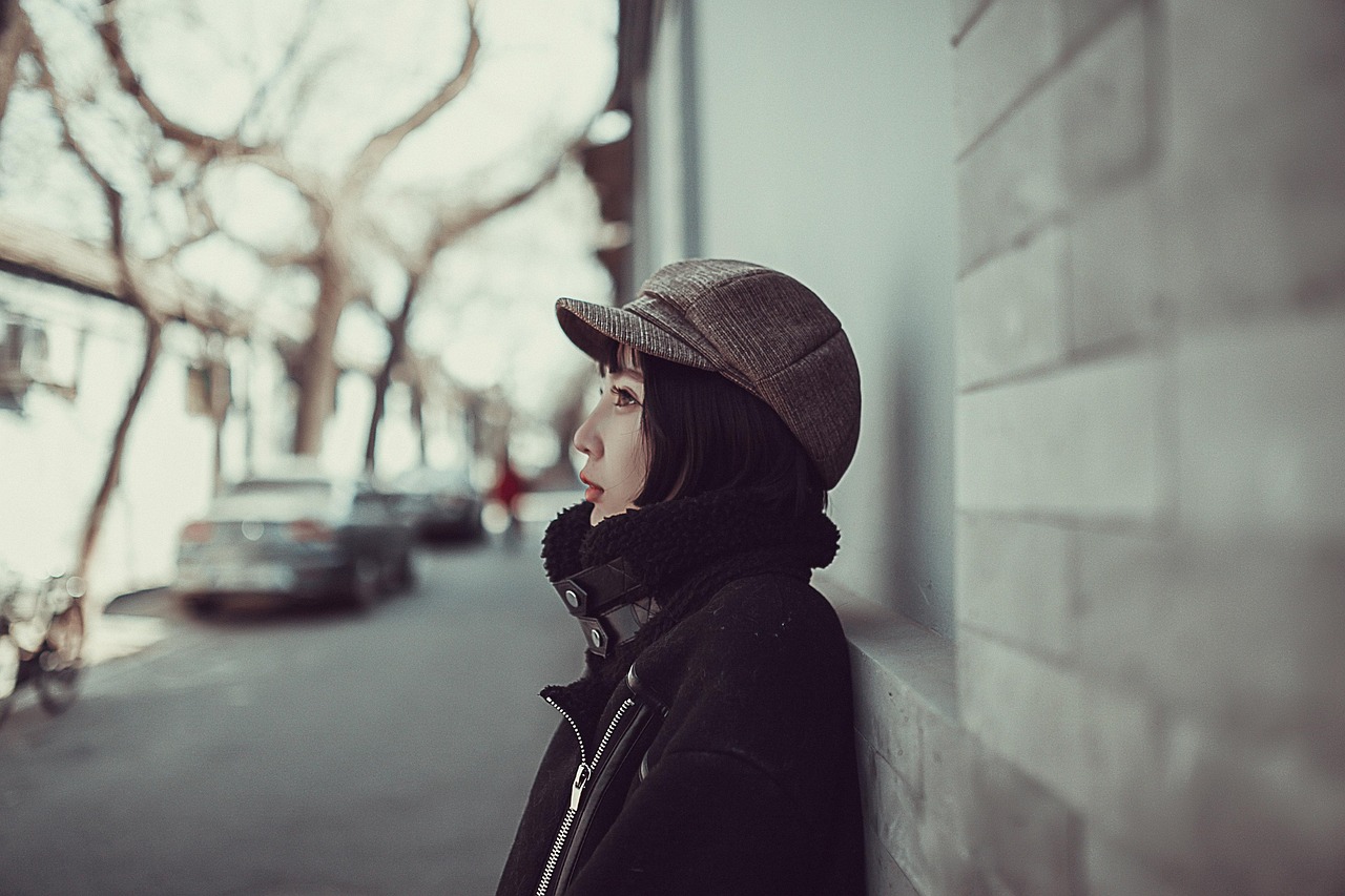 young woman standing up against a building, looking off into the distance