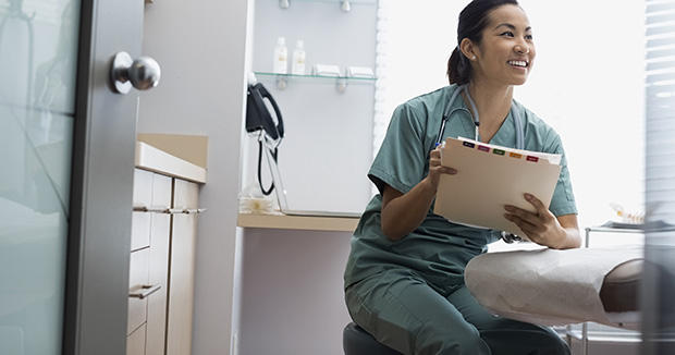 smiling female medical provider wearing scrubs holding a folder while standing in an examination room