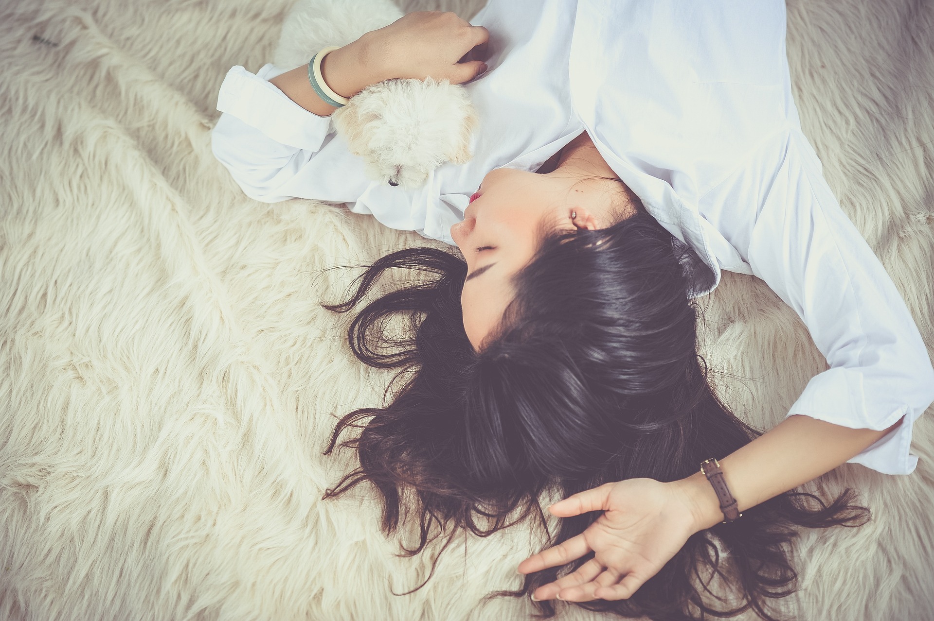 woman with long dark hair lying on bed with small white dog