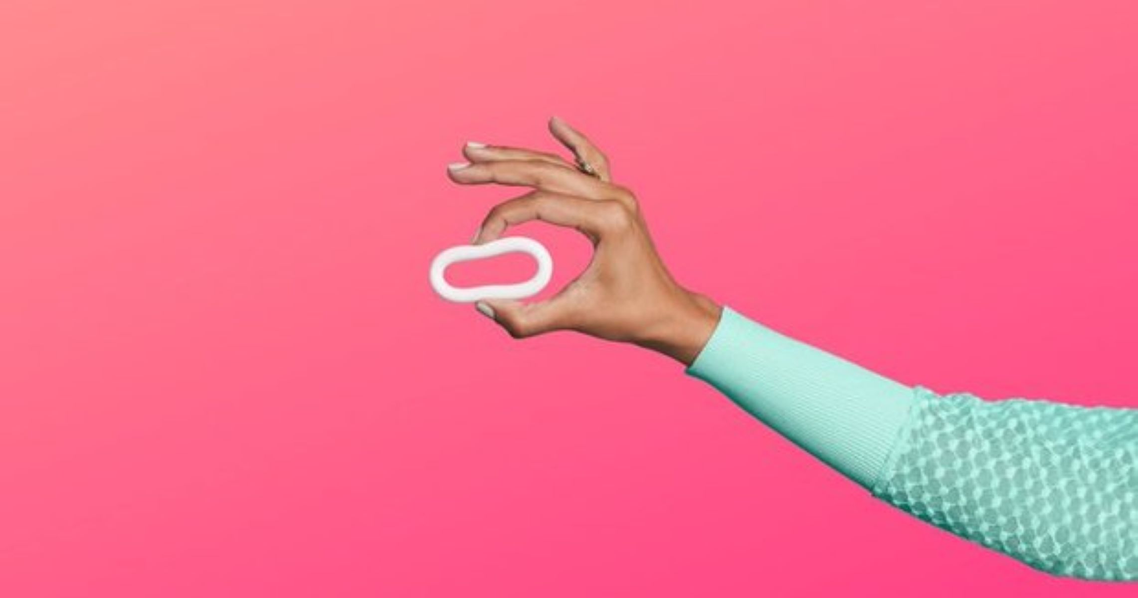 an arm holding up birth control ring with two fingers against a pink background