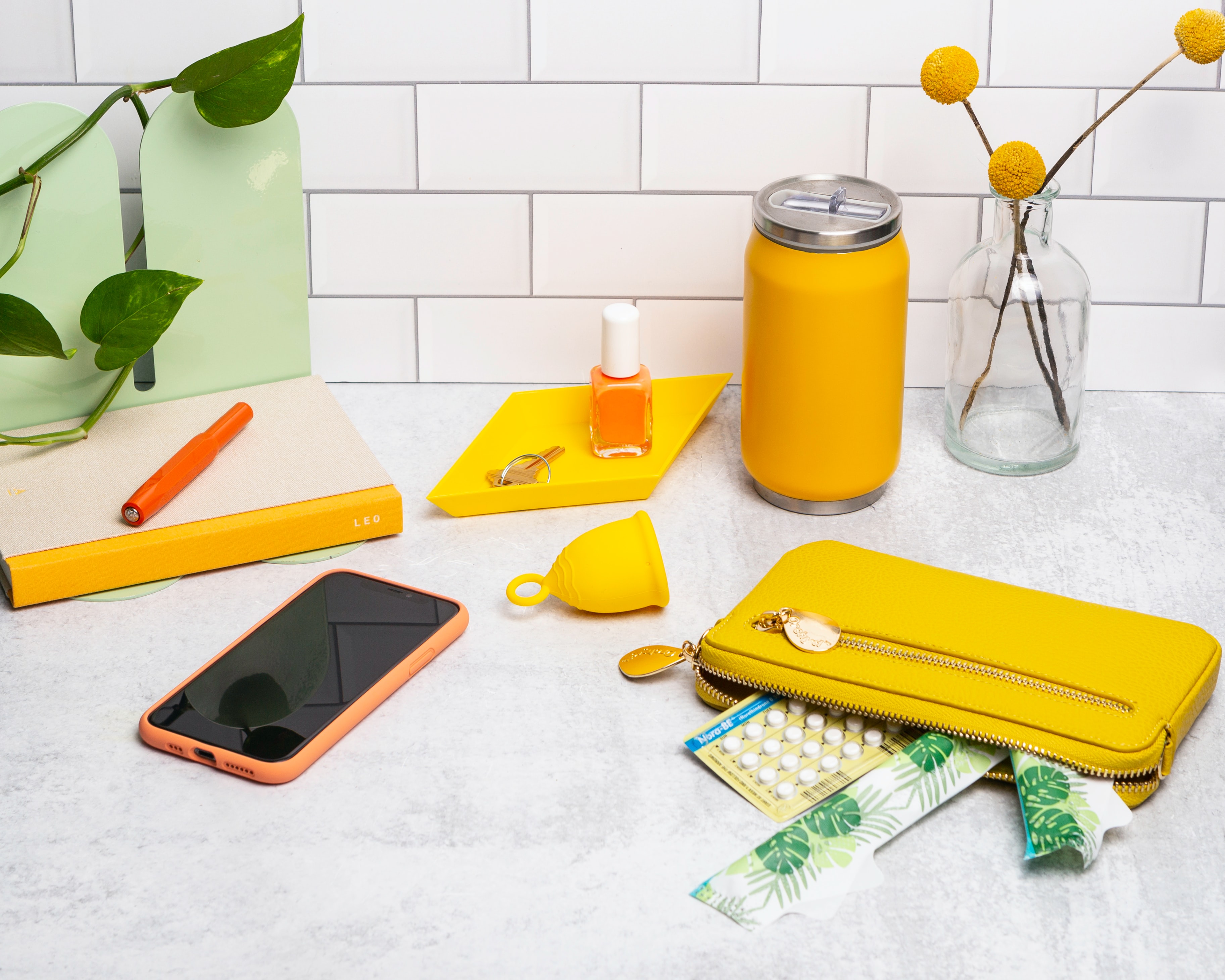 assortment of items on a countertop, including phone, pen, nail polish, tampons, wallet, birth control pills