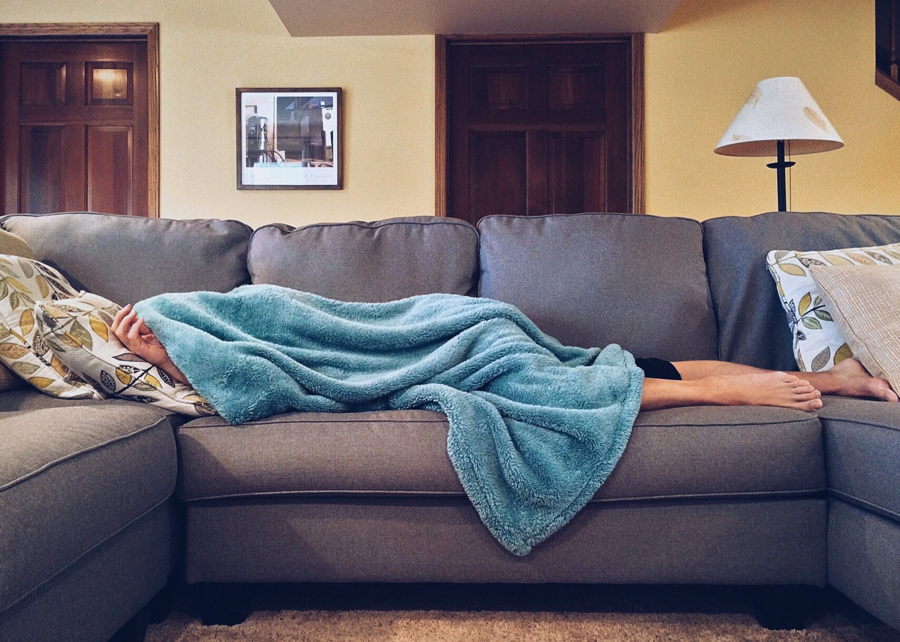woman hiding under a blue blanket while lying on a couch
