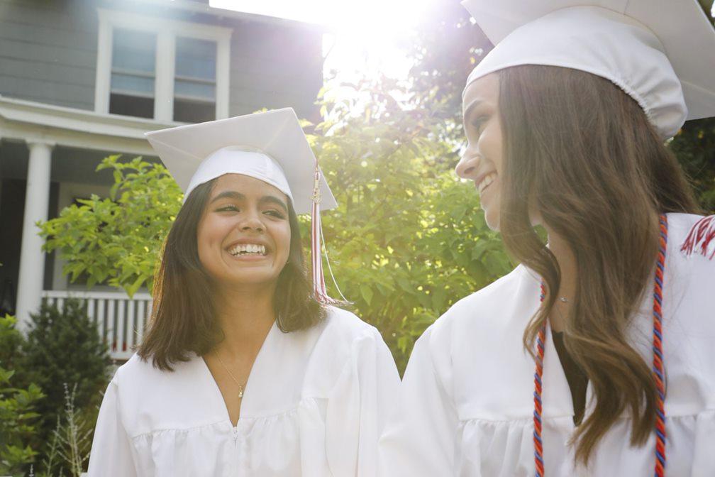 two young people with long dark hair wearing graduation caps and gowns