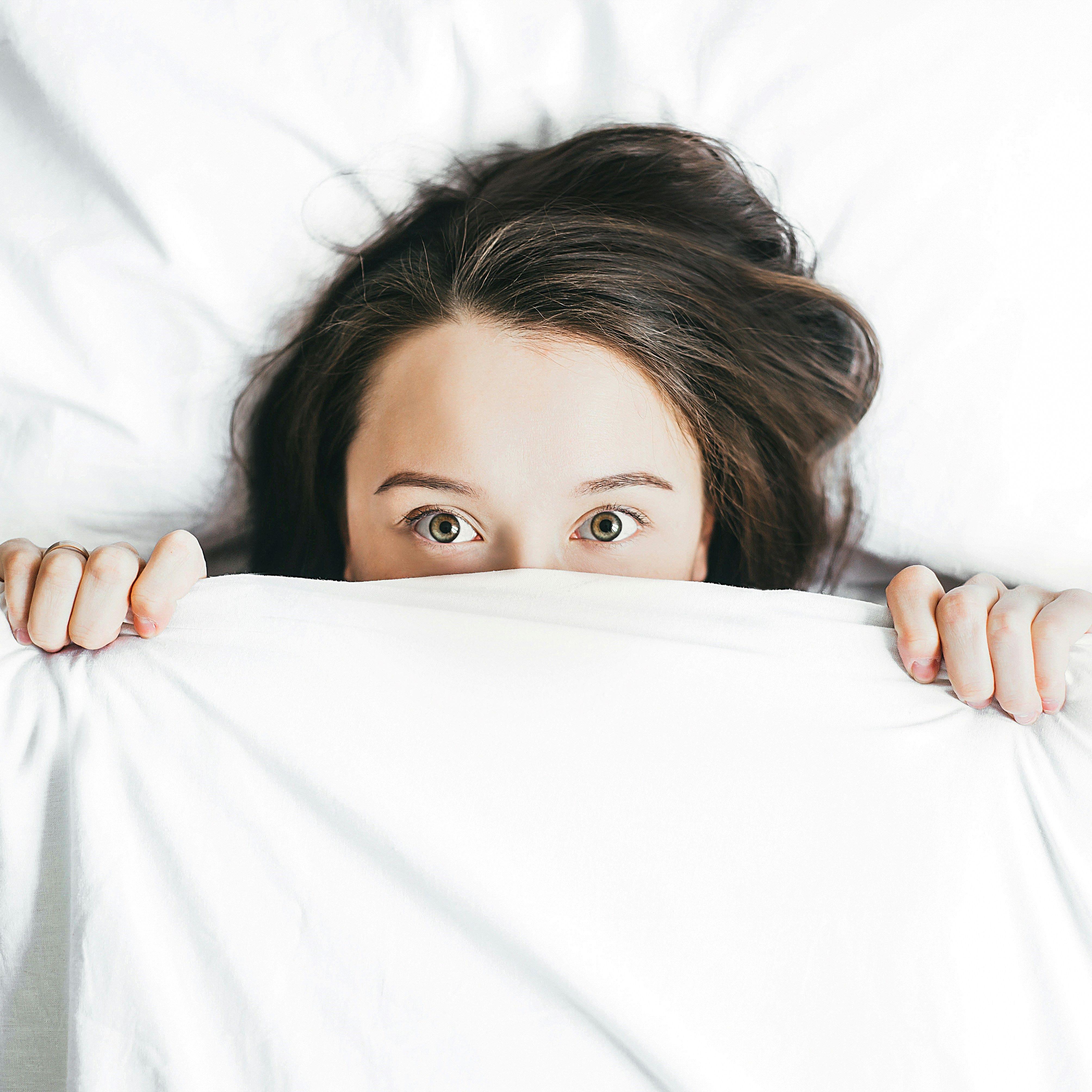 woman with brown hair lying in bed pulling the covers up over her chin