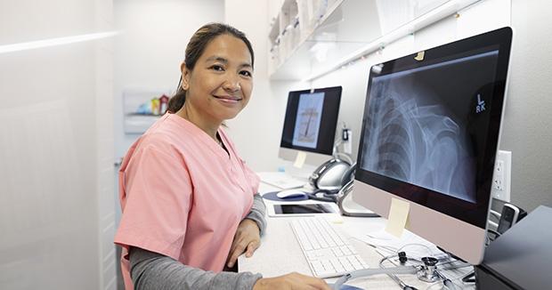 female medical provider wearing pink scrubs looking at an xray on a desktop computer