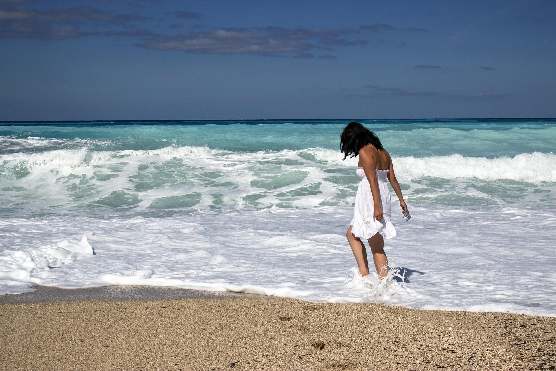 woman in white dress walking on the beach by an ocean