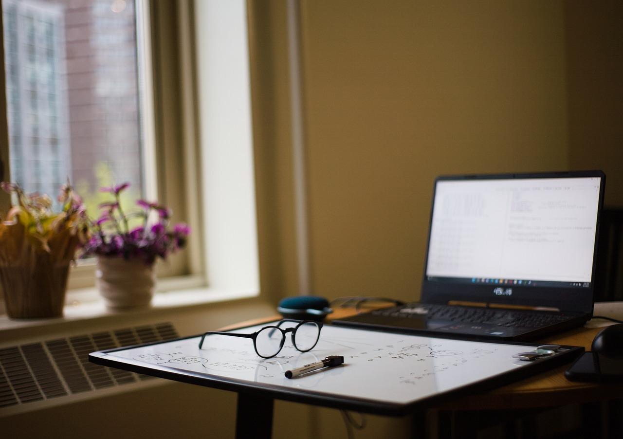 dorm room containing a window, potted plants, a desk, glasses, and a laptop 