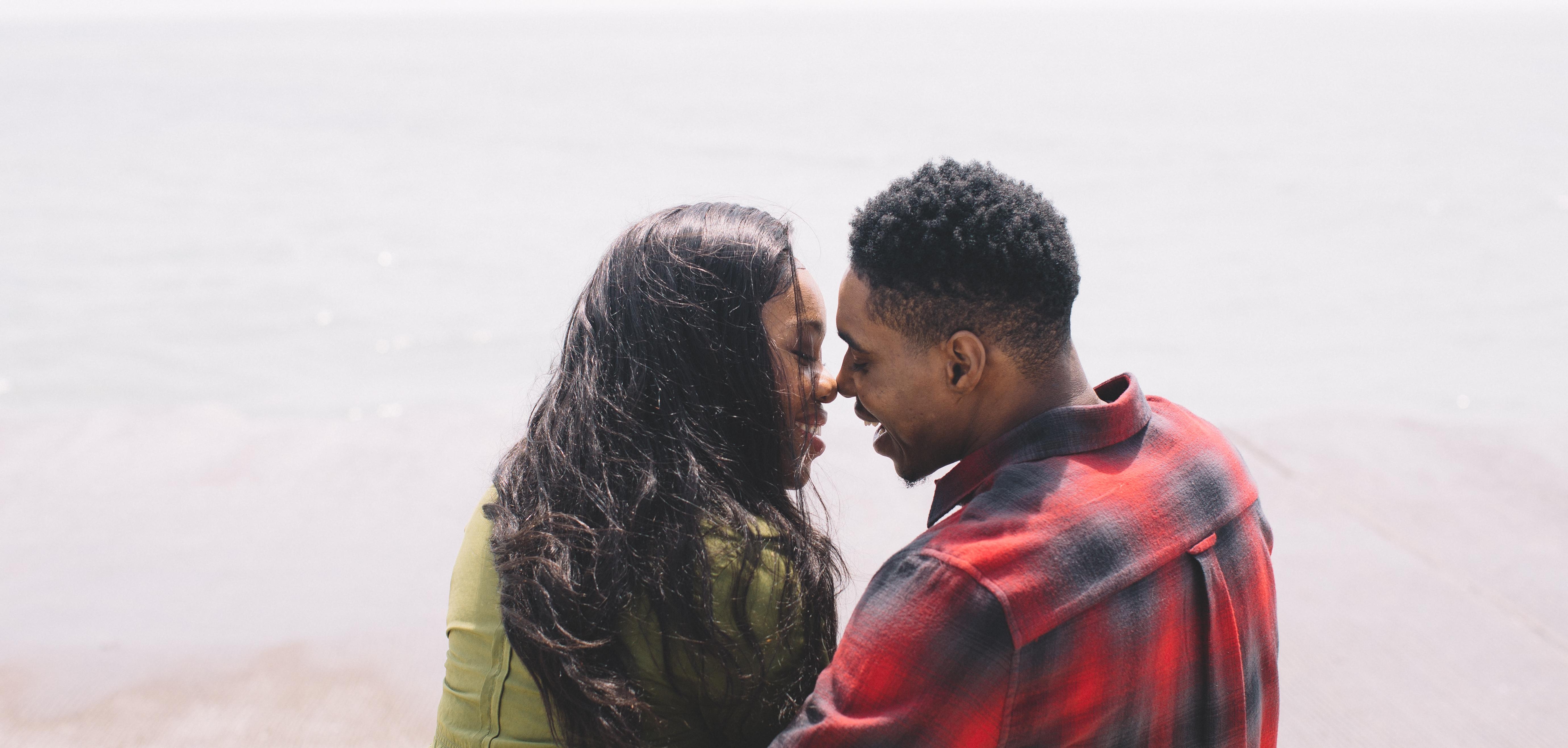 BIPOC woman and BIPOC man smiling and leaning in to kiss