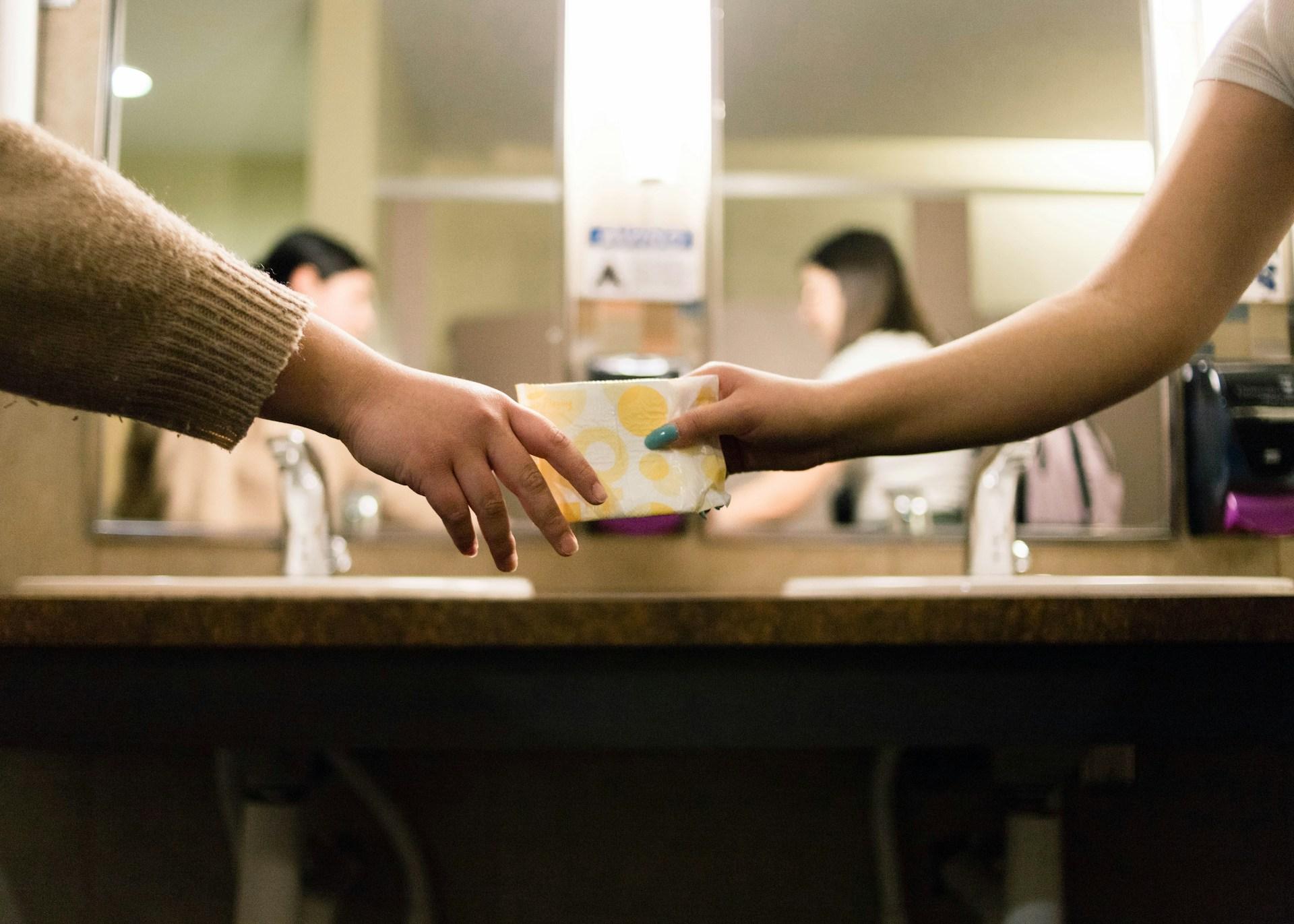 two women exchanging a sanitary pad in a bathroom