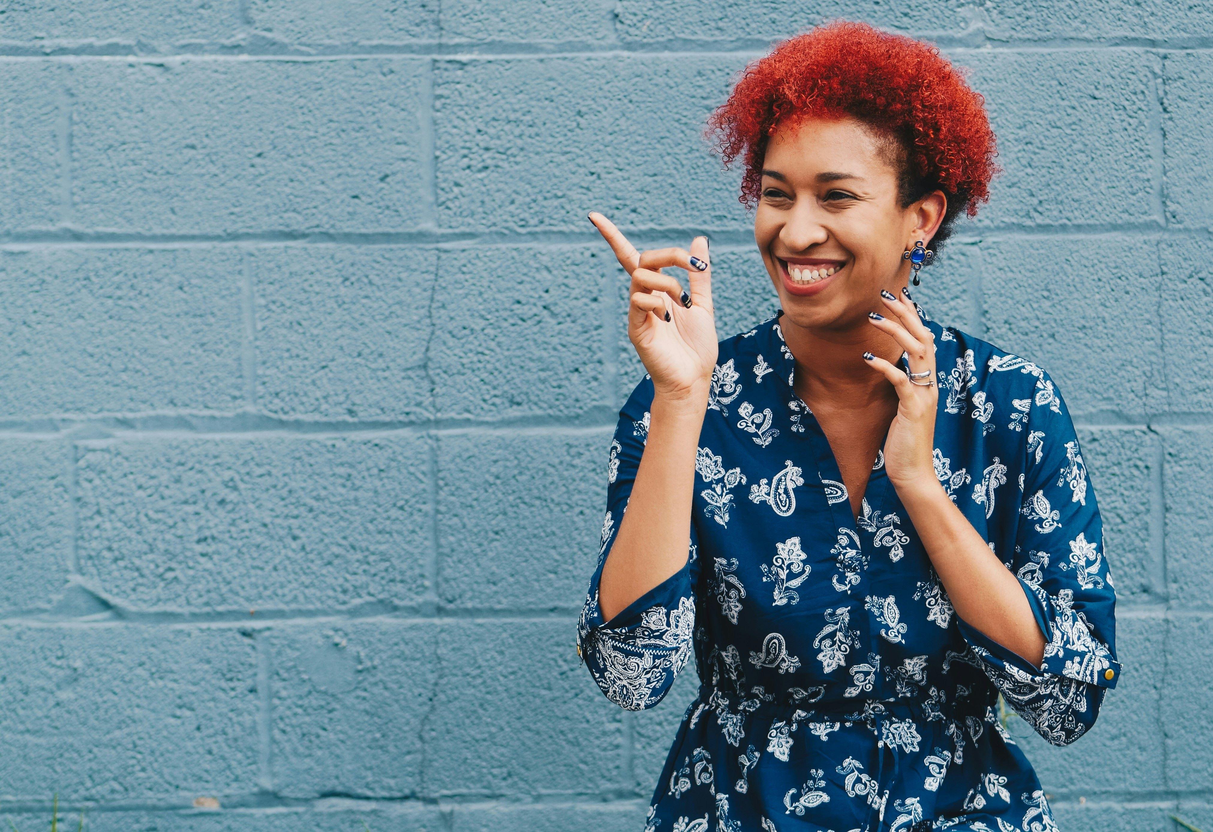 female poc with red hair and a blue shirt pointing and laughin