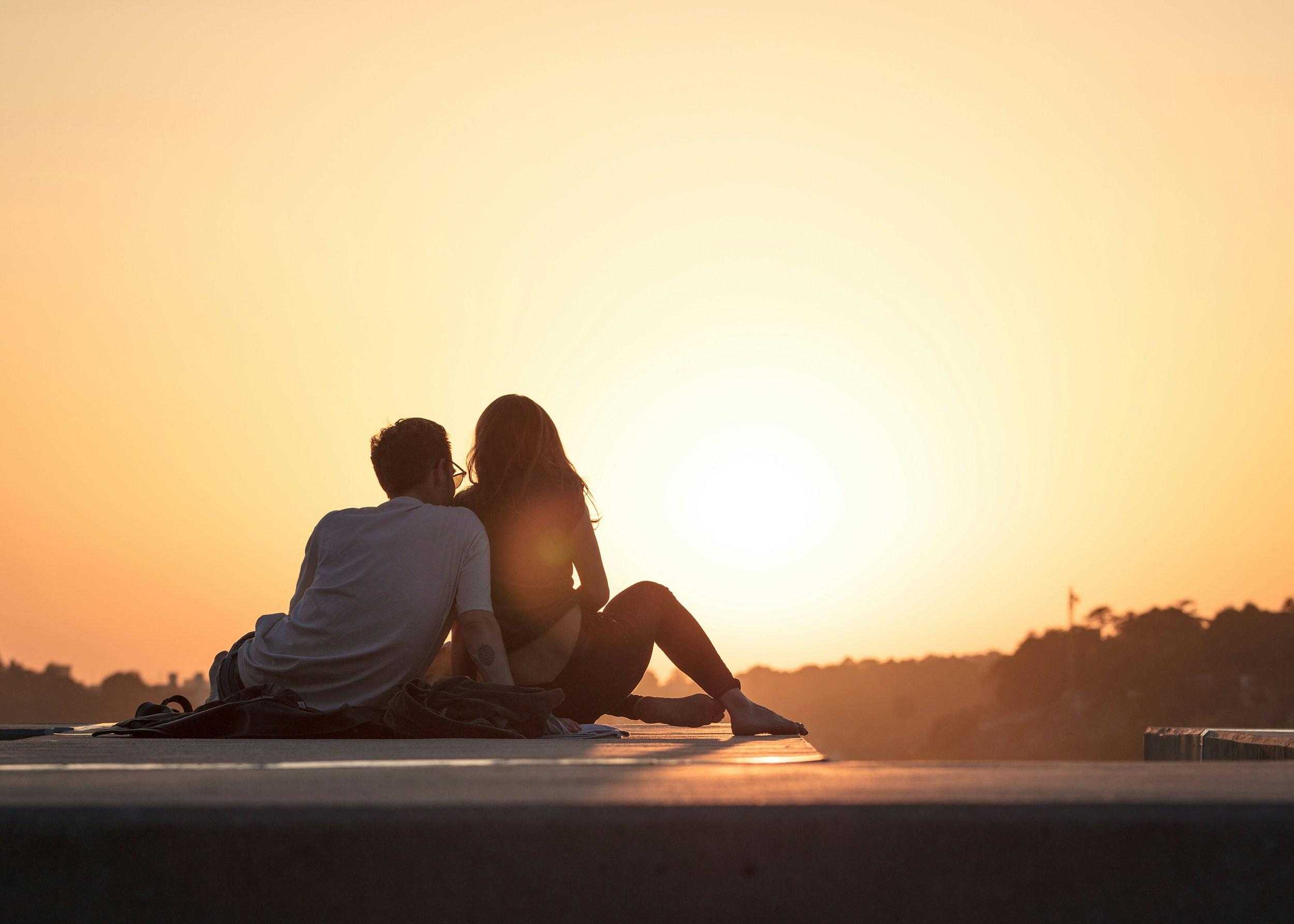 couple sitting and looking at a sunset, snuggling
