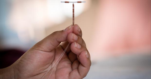 a hand holding an IUD with their thumb, pointer finger and middle finger