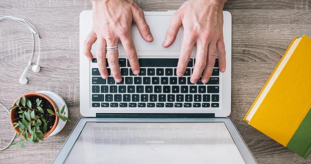 bird's eye view of hands typing on a laptop keyboard next to a potted plant and a pair of headphones