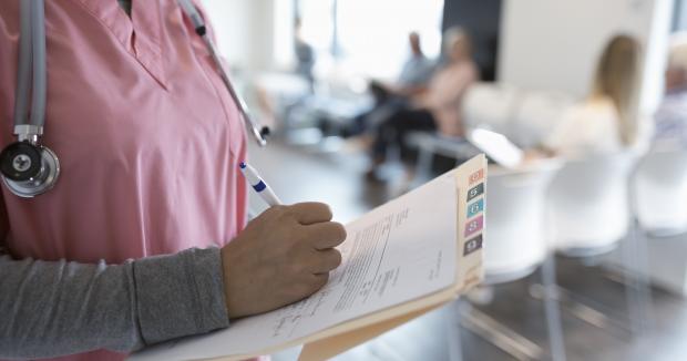 medical provider in pink scrubs writing in a chart