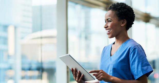 medical provider in blue scrubs holding a tablet and smiling in front of a window