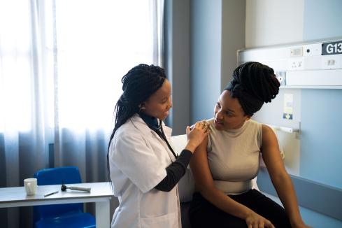 young bipoc female sitting on table in an exam room, talking to a provider in a white coat