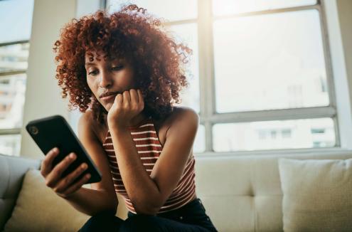 BIPOC woman sitting on the couch looking at her cell phone