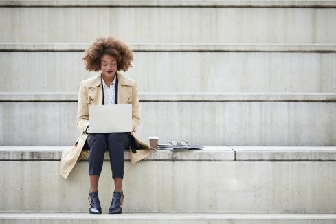 Female BIPOC sitting on a bench using her laptop