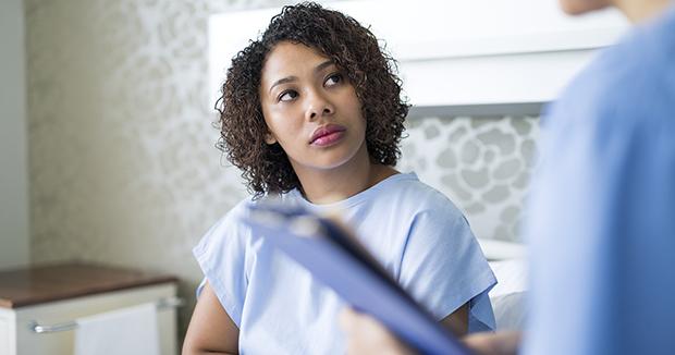 black woman in an exam gown looking at a medical provider in blue scrubs