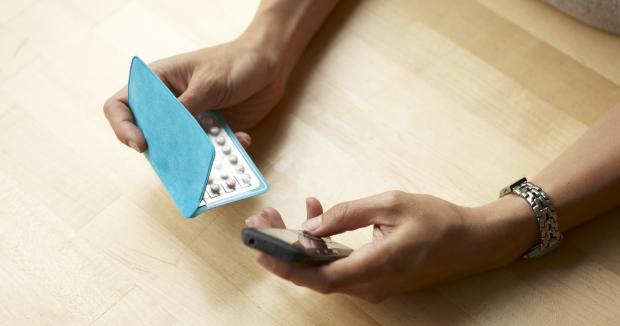 bird's eye view of a person holding a monthly pack of oral contraceptives in one hand and a cell phone in the other