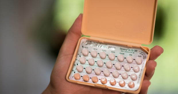 a hand holding an orange monthly pack of oral contraceptives