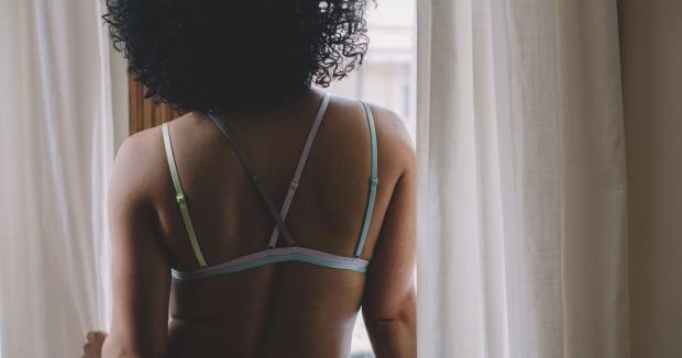 black woman in a bra standing by a window and looking out