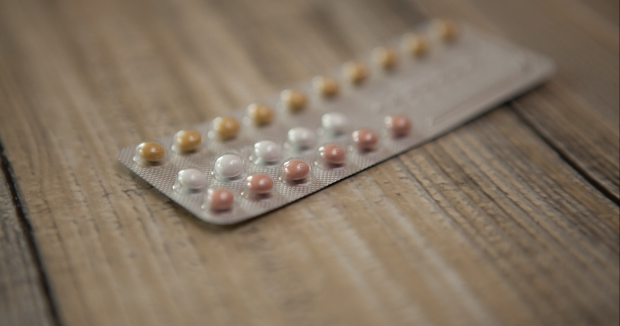 close up of yellow, white, and red oral contraceptives on a wooden surface