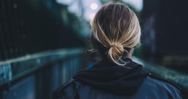 woman with dark blonde hair with a black jacket and hoodie walking away from camera