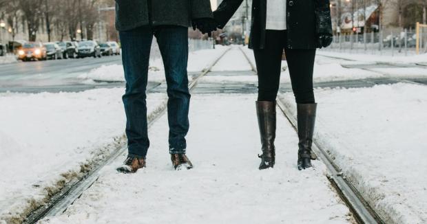 couple shown from the shoulders down holding hands while standing in a city with snow on the ground