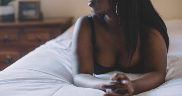 BIPOC woman wearing a bra and lying on her bed while looking to the left