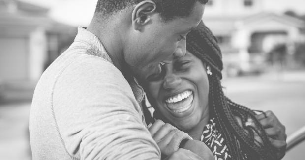 black and white image of BIPOC couple laughing and snuggling on the street