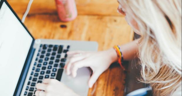 blonde woman using her laptop at a wooden table with a can of soda next to her