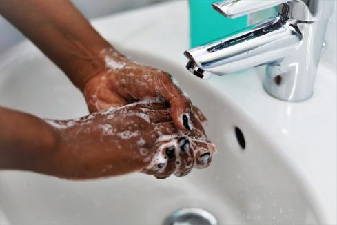 BIPOC washing rubbing soap on their hands in a bathroom sink