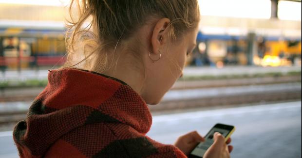 blonde woman in red hooded jacket using her smartphone to send a text