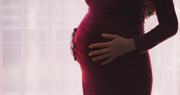 pregnant woman in red dress touching belly with both hands