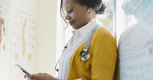 black female medical provider with a stethoscope around her neck using her smartphone