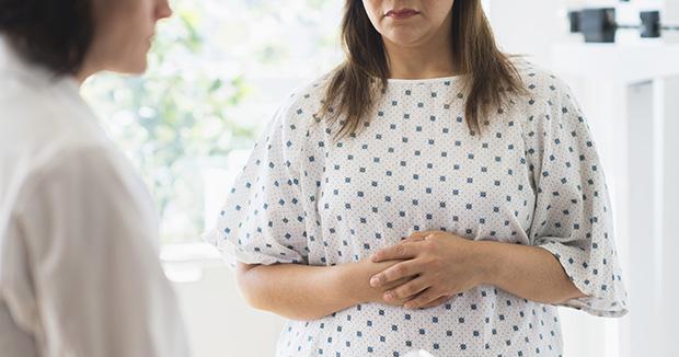 woman with brown hair in a polka dot exam gown talking to a provider with her arms crossed over her stomach