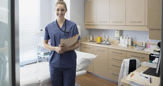 smiling female medical provider wearing scrubs holding a folder while standing in an examination room