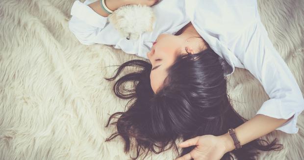 woman with long dark hair lying on bed with small white dog