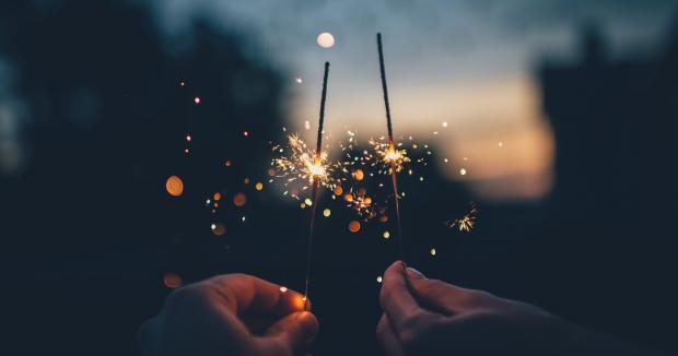 two hands holding lit sparklers at dusk 